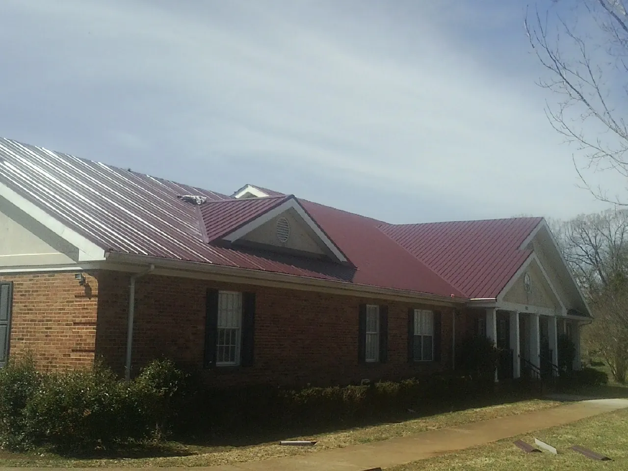 Red metal roof with gabled entries on a long brick building, from a Hail Damage Roof Repair job in Wimauma