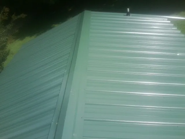 New green metal panels meeting at the ridge of a roof — Flat Roof Repair work by our crew in Wimauma