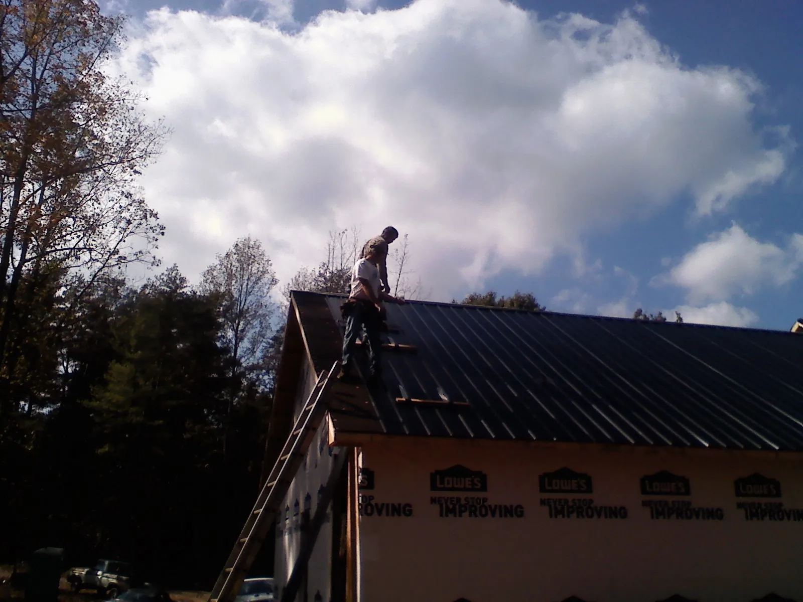 Roofer fastening dark metal panels high against a cloudy sky, from a Roof Inspection job in Wimauma