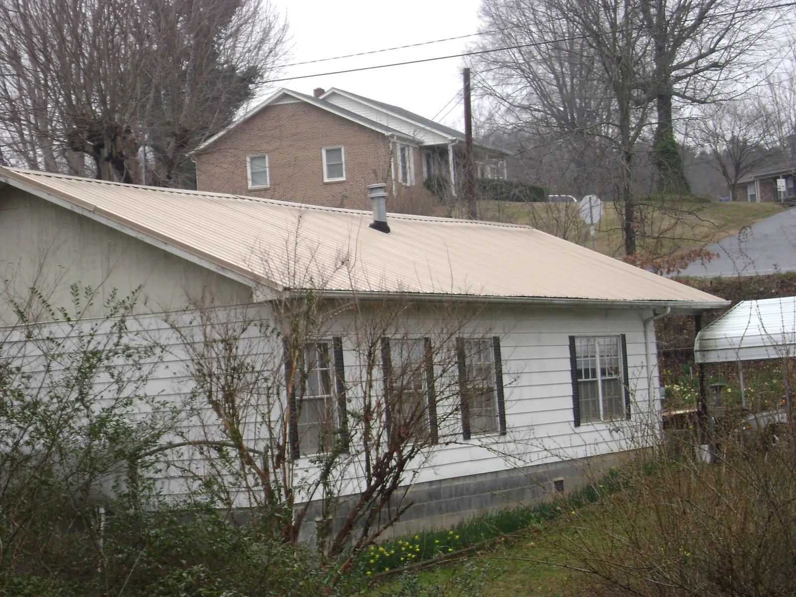 Tan metal roof on a white sided house set into a hillside — Commercial Roofing by Roofing Brothers in Wimauma